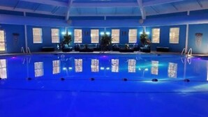 Une piscine intérieure aux parois bleues, entourée d’espaces de détente et de grandes fenêtres.