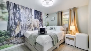 Une chambre à coucher avec un lit, une table de chevet, une lampe, une fresque murale et une fenêtre avec des rideaux.