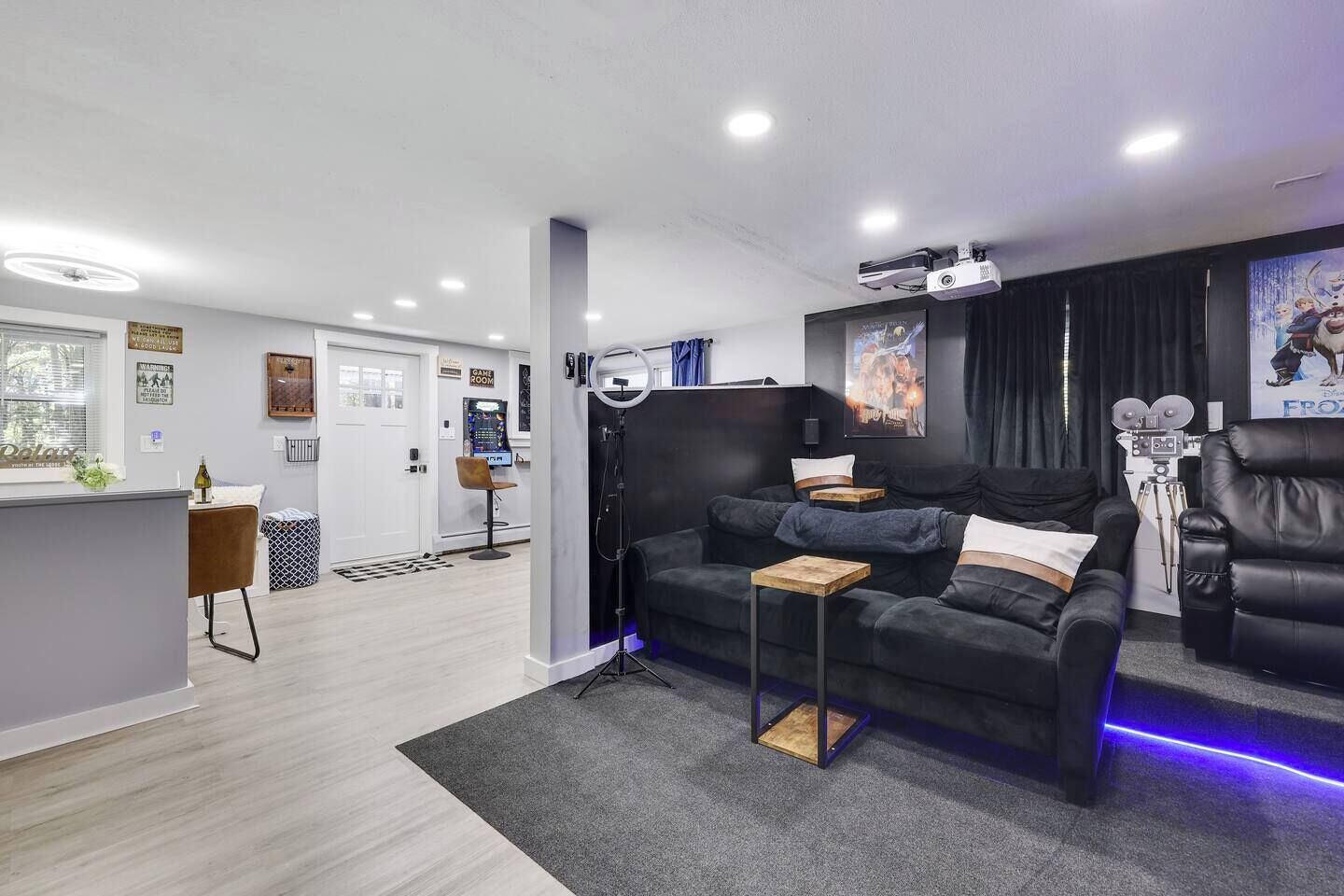 Un salon moderne avec un canapé noir, une table basse et un espace dédié aux jeux vidéo, comprenant un écran et un fauteuil.