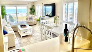 A spacious living area with a balcony overlooking the sea, a flat-screen TV, and a dining table with chairs. - Book Sailfish Sands Now! Oceanfront 3BR + Amazing Views & Special Deals (Cocoa Beach)