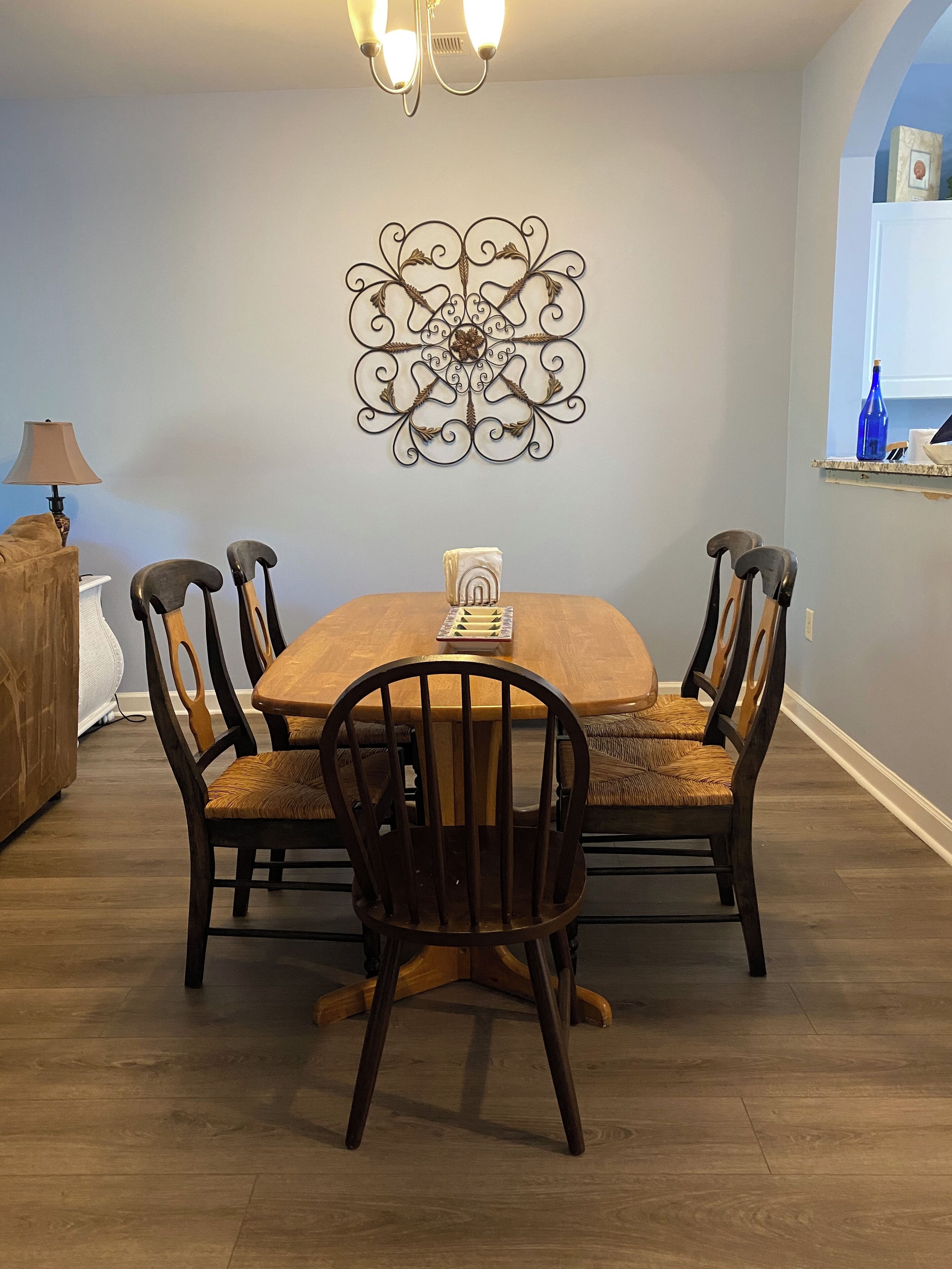 Un comedor con una mesa y sillas de madera, un adorno en la pared y una lámpara.