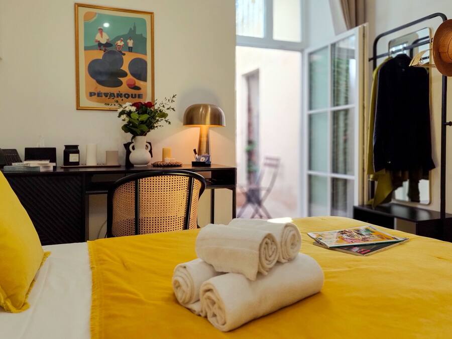 Une chambre d’hôtel avec une couvre-lit jaune, des serviettes roulées, un bureau avec une lampe, une chaise et une affiche accrochée au mur.