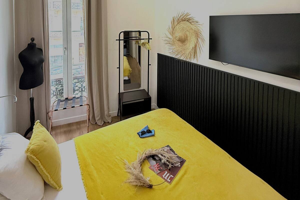 A modern hotel room with a bed, a TV, a window with curtains, a mirror, and a mannequin.