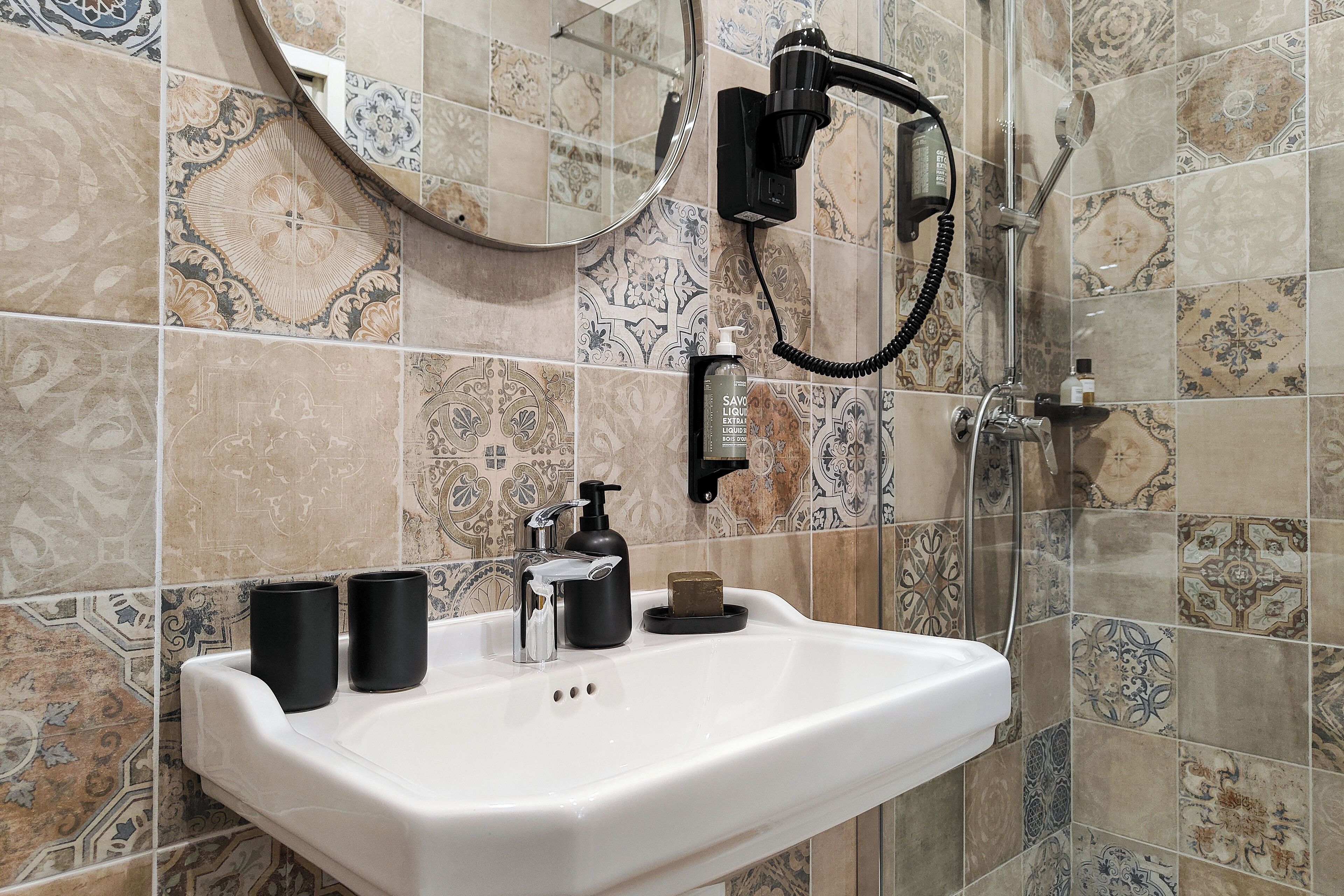 A bathroom with a white sink, black soap dispenser, and a hairdryer mounted on the wall.