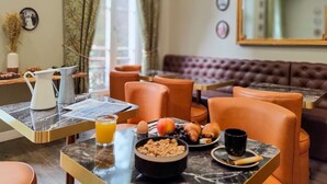 A breakfast setting with a marble table, orange chairs, a brown sofa, and a breakfast spread including croissants, fruit, and cereal. - Boutique Hôtel Provencia (Marseille)