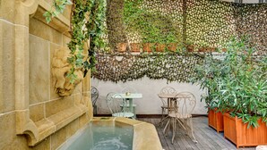 A stone fountain with a lion head, surrounded by potted plants and outdoor seating. - Boutique Hôtel Provencia (Marseille)