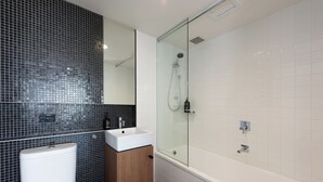Un baño moderno con inodoro, lavamanos y cabina de ducha con mampara de vidrio.