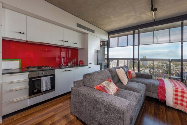 A modern kitchen with white cabinets, a red backsplash, and a large window overlooking a cityscape.
