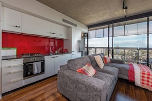 A modern kitchen with white cabinets, a red backsplash, and a large window overlooking a cityscape.
