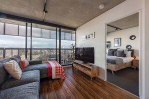 A modern living room with a large TV, a sofa, and a balcony with a city view.