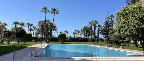 Ein Schwimmbecken mit Fliesen und einer umlaufenden Terrasse, umgeben von Palmen und Grünpflanzen.
