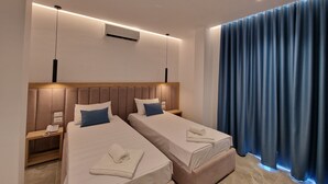 A hotel room with two beds, a wooden headboard, a telephone on a bedside table, and a blue curtain. - Monel Hotel (Ksamil)