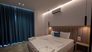 A modern hotel room with a large bed, a wooden nightstand, and a built-in air conditioning unit. - Monel Hotel (Ksamil)