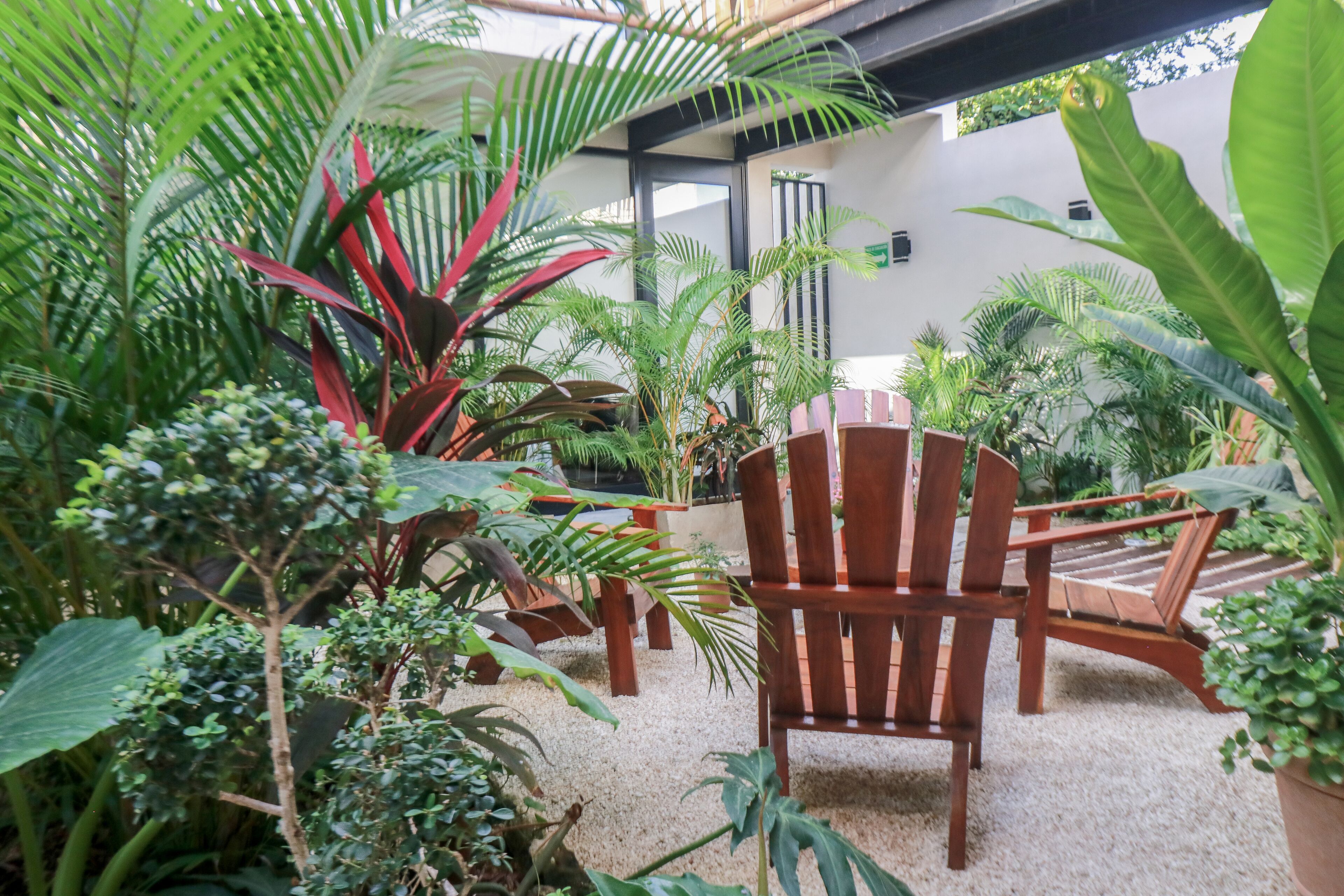 Un espace patio aménagé avec des chaises et des tables en bois, entouré d’une végétation tropicale luxuriante.