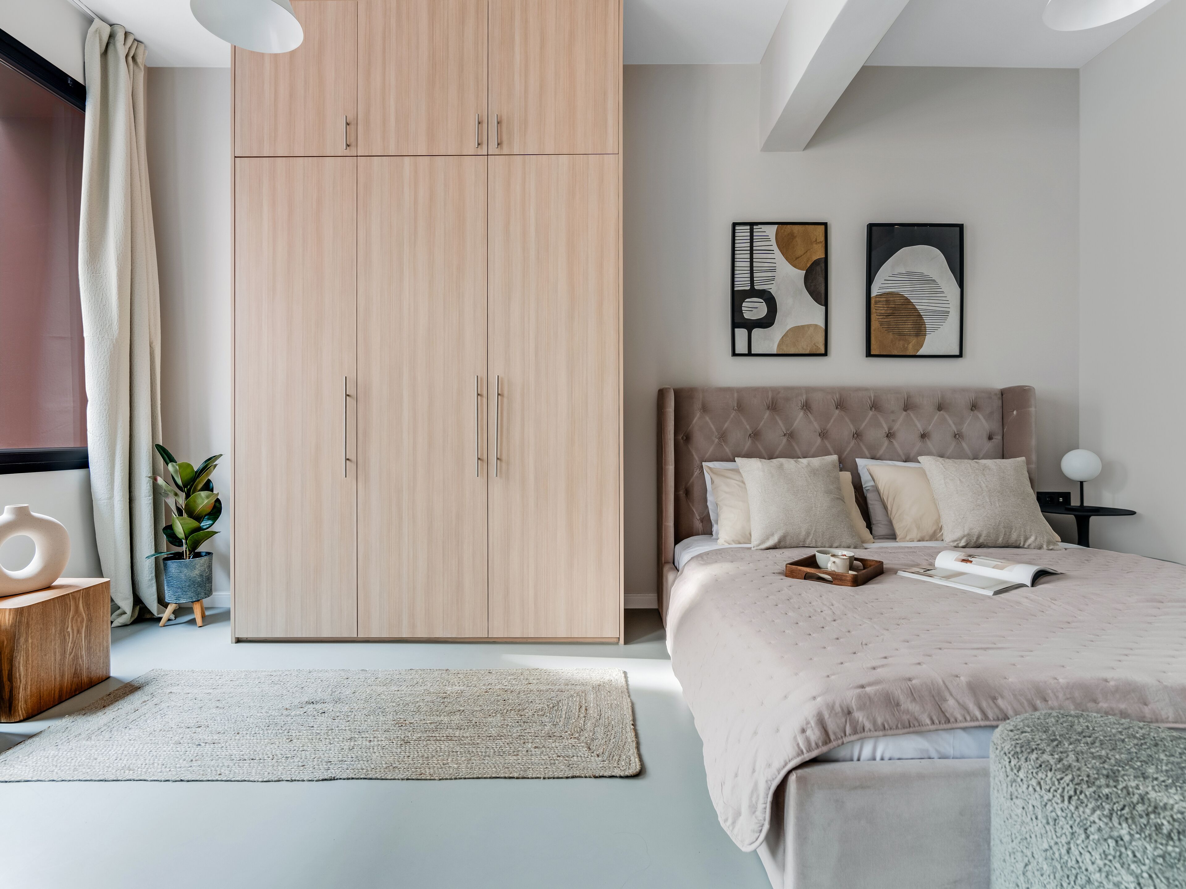 Ein Schlafzimmer mit großem Kleiderschrank, einem Bett mit vielen Kissen, einem Nachttisch mit Lampe und zwei Wandbildern.