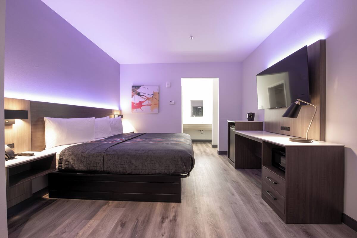 Quarto moderno com cama, mesas de cabeceira, escrivaninha e televisão.