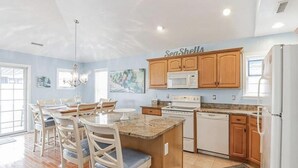 Una cocina con armarios de madera, encimera de granito, refrigerador blanco y un comedor con candelabro.