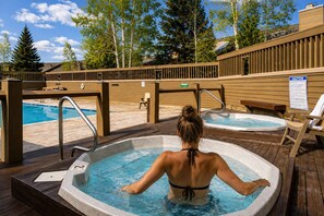 A person relaxing in a hot tub with a pool and lounge chairs in the background. - Deer Valley Adventure Retreat with Free Ski Shuttle 1791 (Park City)