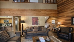 Un vaste espace de vie doté d’un haut plafond, de murs en bois, d’un ensemble de canapés, d’une table basse et d’un coin repas avec une lampe.
