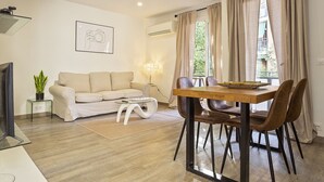 Ein modernes Wohnzimmer mit einer Couch, einem Esstisch mit Stühlen, einem Fernseher, einer Pflanze und einer Lampe.