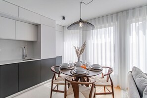 Una cocina moderna con armarios blancos, una mesa de comedor dispuesta con platos, vasos y un florero con ramas.