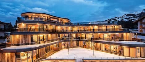 Un hotel de varios pisos con fachada curva, amplios ventanales y suelo cubierto de nieve.