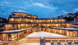 Een meerlaags hotel met een gebogen gevel, grote glasramen en een met sneeuw bedekte grond.
