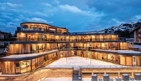 Un hotel de varios pisos con fachada curva, amplios ventanales y suelo cubierto de nieve.