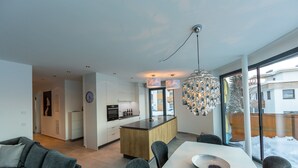 Une cuisine moderne dotée d’un îlot central, d’un coin repas avec une table et des chaises blanches, et d’une grande fenêtre offrant une vue sur l’extérieur.