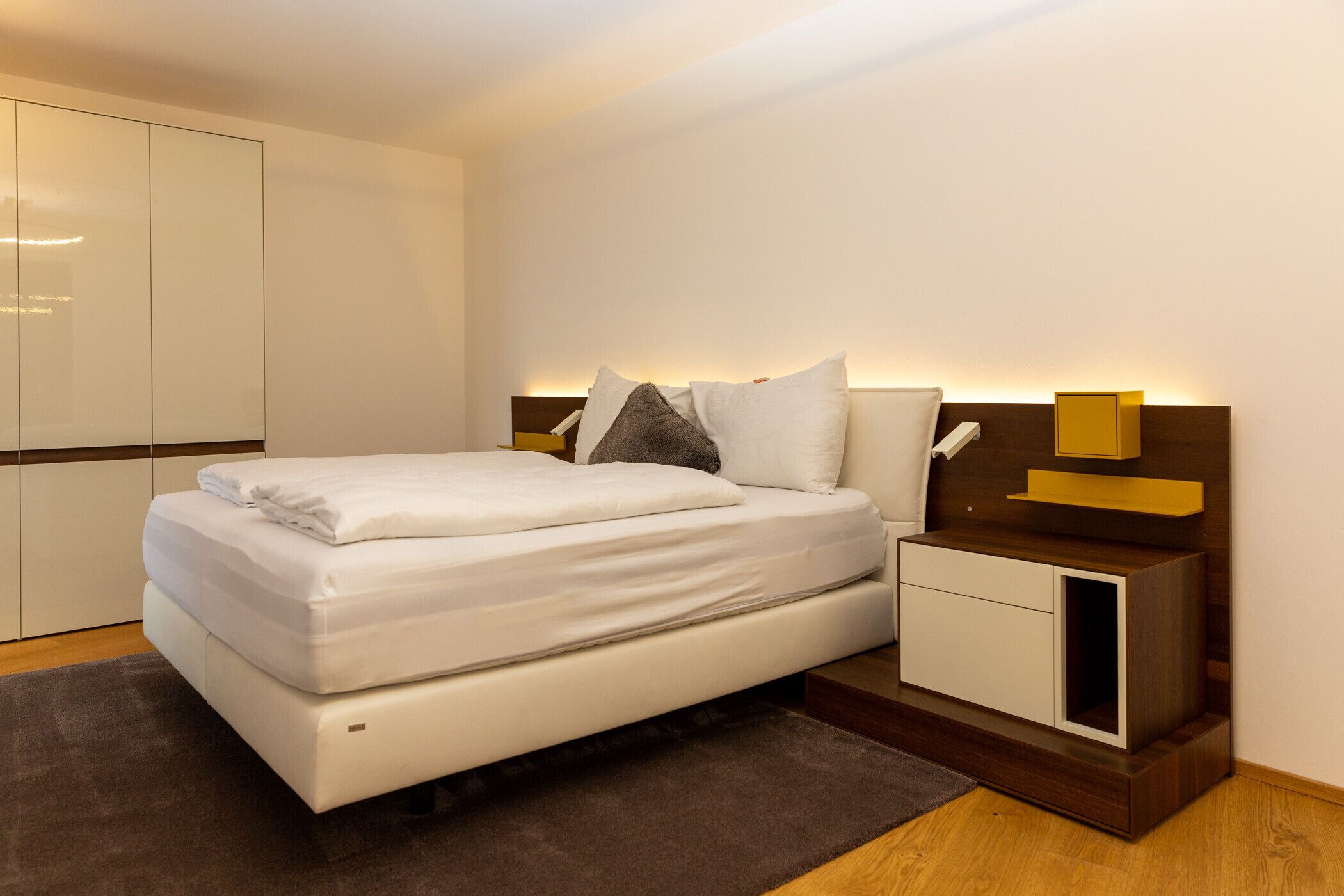 A modern bedroom with a large bed, bedside tables, and a wardrobe.