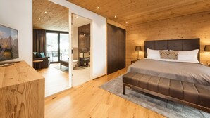 A modern bedroom with a wooden ceiling, a large bed with a headboard, a bench, and a view of a balcony. - Chalet Alpin Jewel T7 (Kirchberg in Tirol)
