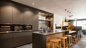 A modern kitchen with a central island, bar stools, and built-in appliances. - Chalet Alpin Jewel T7 (Kirchberg in Tirol)