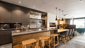 A modern kitchen with a central island, bar stools, and a dining area with a table and chairs. - Chalet Alpin Jewel T7 (Kirchberg in Tirol)