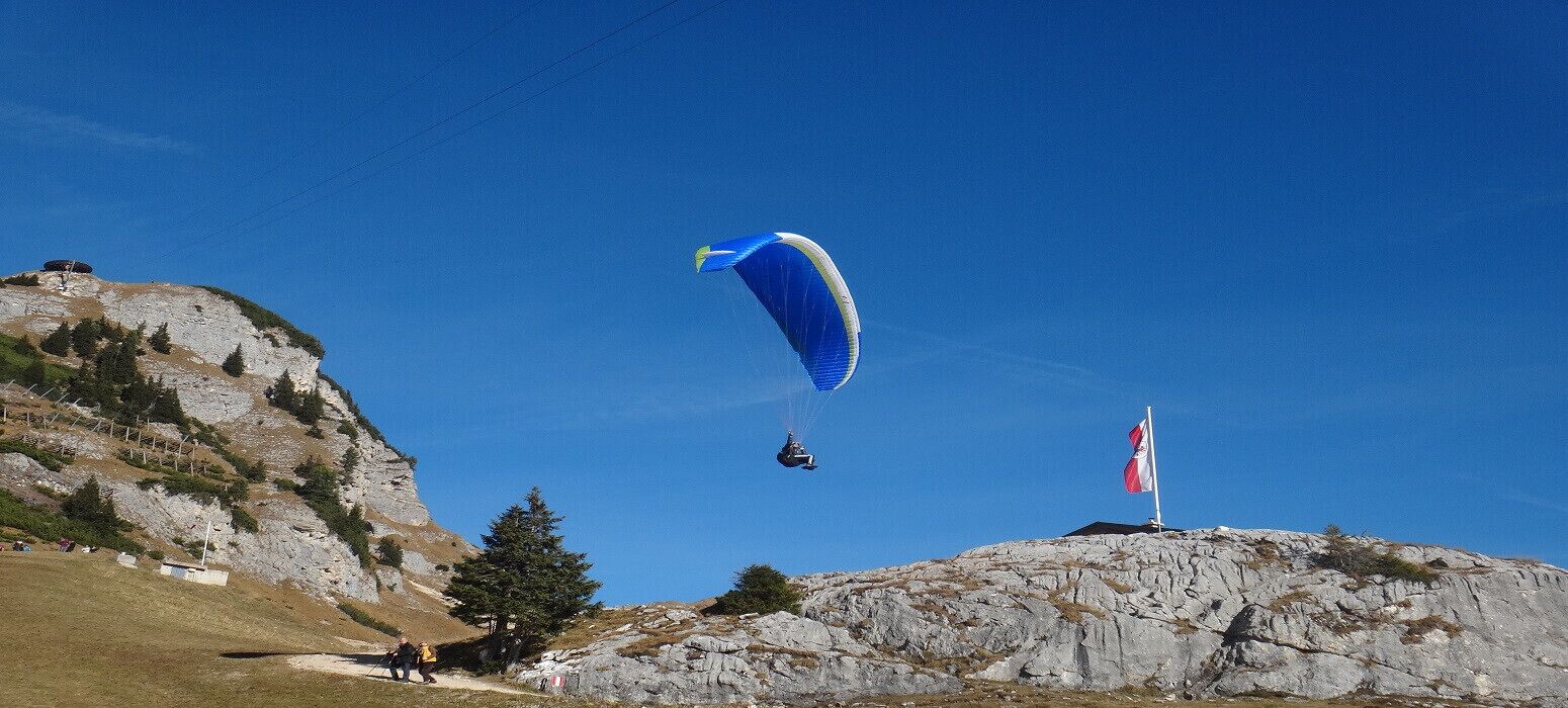 Une personne pratiquant le parapente au-dessus d’une colline rocheuse, un drapeau flottant au sommet.