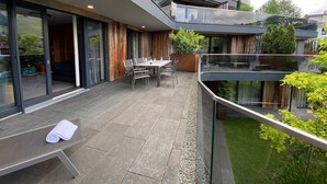 A modern house with a patio, a dining area, and a glass balustrade overlooking a garden. - Chalet Alpin Jewel T7 (Kirchberg in Tirol)