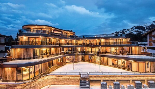 A multi-story hotel with a curved facade, large glass windows, and a snow-covered ground.