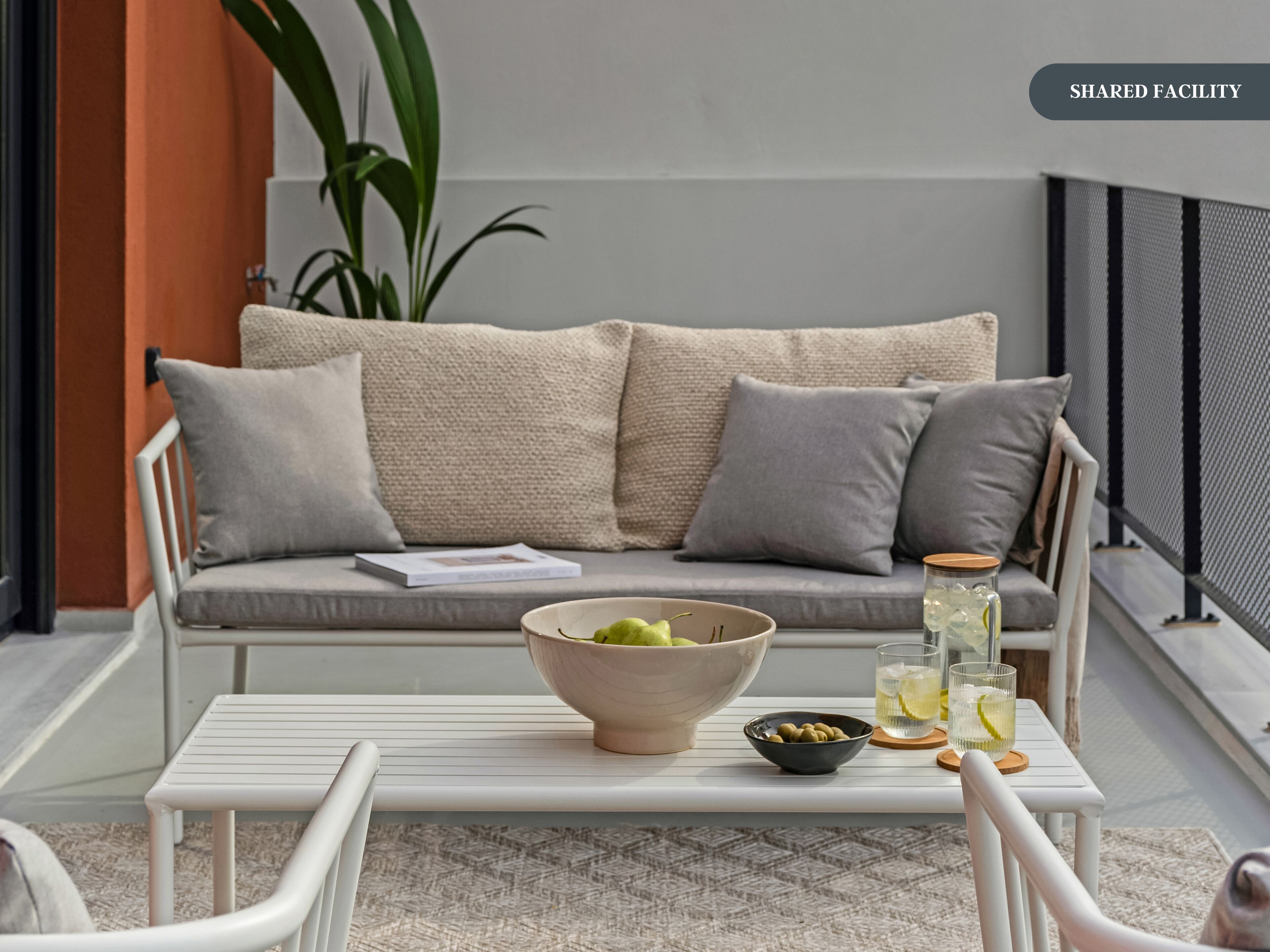 A shared facility with a sofa, a table with a bowl of fruit, a glass of drink, and a bowl of olives.