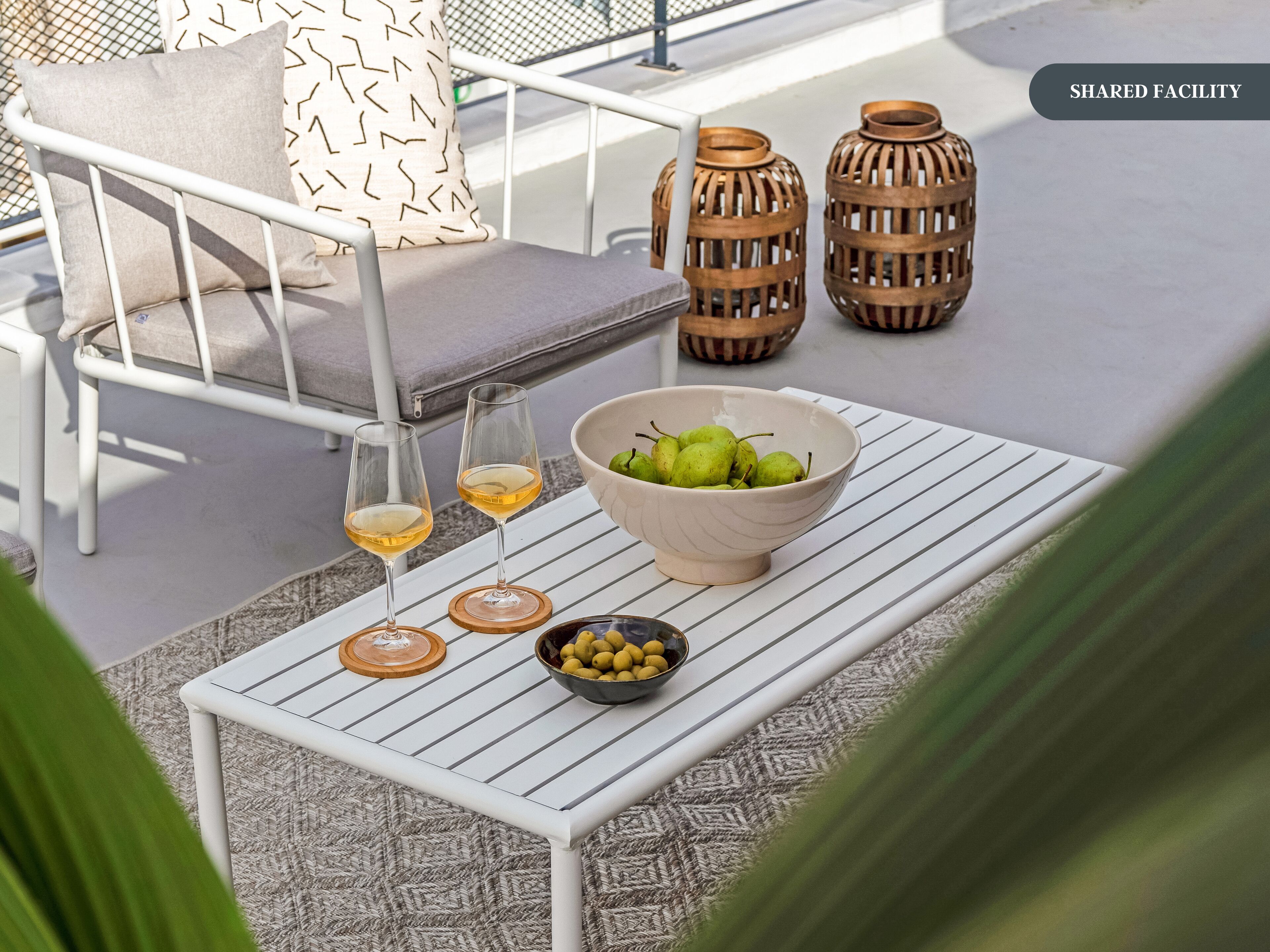 A shared facility with a white metal table, two glasses of white wine, a bowl of green pears, and a bowl of yellow lemons.
