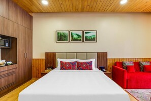 A hotel room with a bed, a red sofa, a wooden wardrobe, and a wall-mounted TV. - Club Mahindra Janjehli Resort (Thunag)