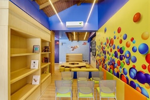 A children's playroom with shelves, a table, chairs, and a colorful wall mural. - Club Mahindra Janjehli Resort (Thunag)