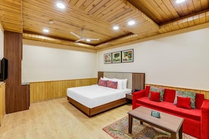 A bedroom with a wooden ceiling, a bed, a red sofa, a nightstand, and a television. - Club Mahindra Janjehli Resort (Thunag)