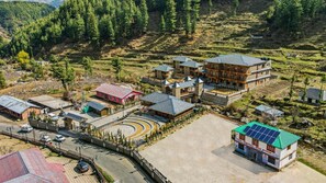 A multi-story building with a central courtyard, surrounded by terraced fields and forested hills. - Club Mahindra Janjehli Resort (Thunag)