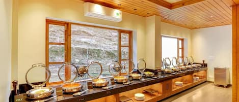 A buffet setup with multiple food stations, a wooden ceiling, and large windows with a view of a mountainous landscape.