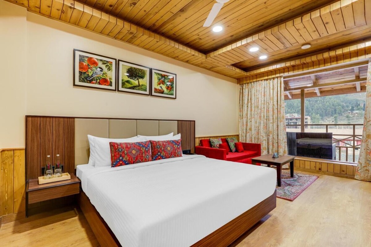A hotel room with a large bed, a red sofa, a TV, and a balcony with a view.