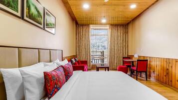 Habitación de hotel con una cama grande, techo de madera, una ventana con cortinas y una pequeña mesa con sillas.