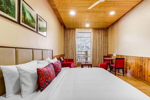 A hotel room with a large bed, a wooden ceiling, a window with curtains, and a small table with chairs. - Club Mahindra Janjehli Resort (Thunag)