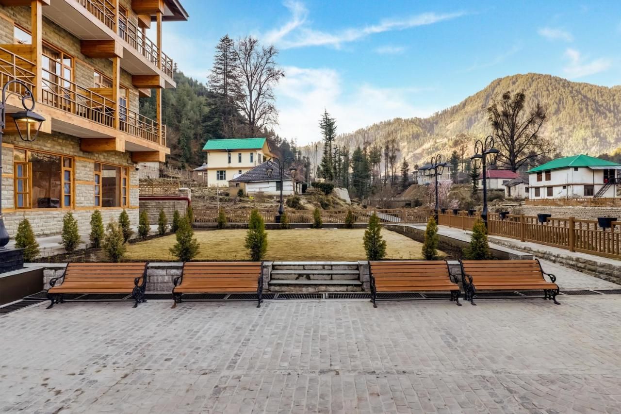 Un patio con bancos, un edificio con balcones y un paisaje montañoso de fondo.