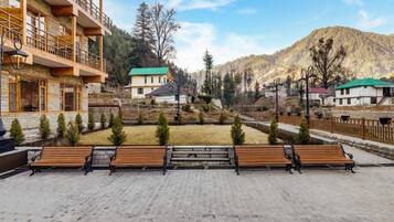 Un patio con bancos, un edificio con balcones y un paisaje montañoso de fondo.