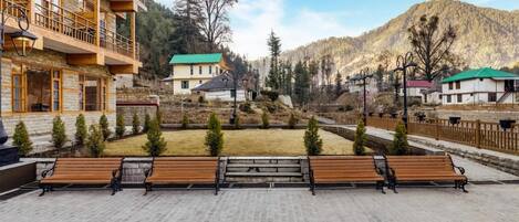 Un patio con bancos, un edificio con balcones y un paisaje montañoso de fondo.