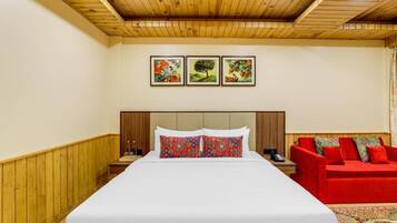 Una habitación de hotel con una cama grande, un sofá rojo y tres cuadros en la pared.